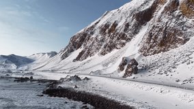 Aerial drone gliding low to the ground and winter snow covered shoreline and ocean sea water with a highway or a road on the right with a large and steep Norway mountains besides of it. Beach waves. - Powered by Shutterstock - Get 15% off with code: PIKWIZARD15