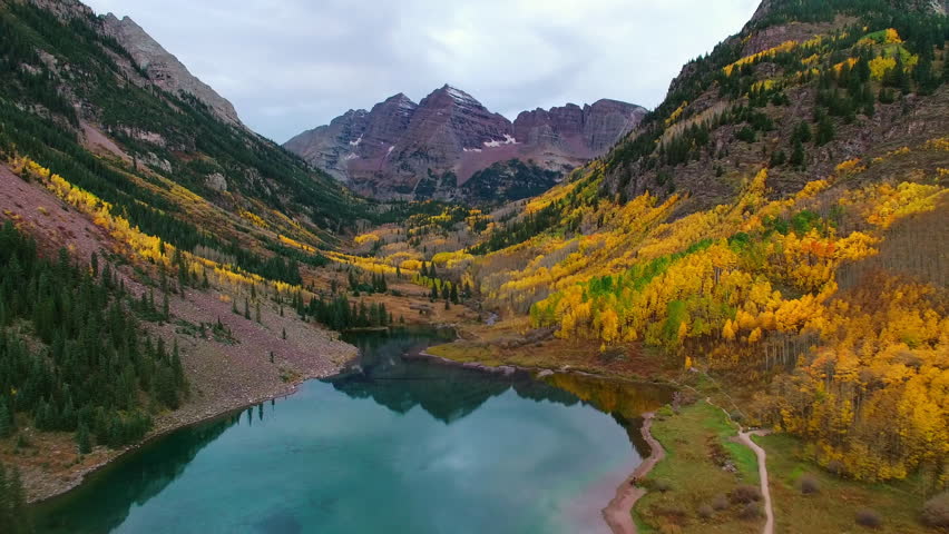 Aerial Shot Of Maroon And North Maroon Peak Under Clouds, Drone Flying Forward Over Lake - CO, Colorado Springs, United States of America