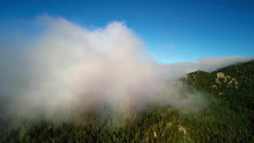 Aerial Forward Shot Of Clouds Moving Over Green Forest Trees On Tranquil Mountains Against Clear Sky - CO, Colorado Springs, United States of America
