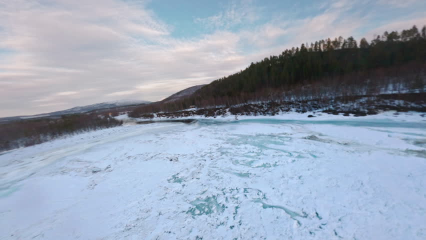 Frozen Målselvfossen river with snow-covered ice and surrounding winter forest