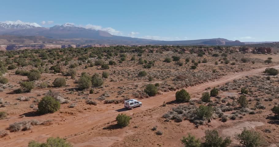 Vehicle makes its way along rough dirt road in remote desert landscape, aerial