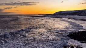 Aerial drone gliding and flying closely over wavy ocean arctic sea water during vibrant orange sunset or sunrise in Norway with mountains in the background with some white clouds. Water reflecting sun - Powered by Shutterstock - Get 15% off with code: PIKWIZARD15