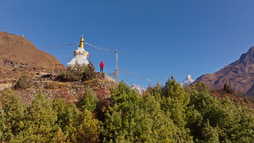 Mountain panorama revealing snow capped Himalayan peaks, meditating traveler facing Mount Everest near ancient Buddhist stupa in Namche Bazaar, Nepal