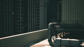 An industrial rooftop features pipes and a low wall overlooking a bustling urban skyline at dusk. City lights twinkle as the sun sets beyond the horizon, casting shadows. - Powered by Shutterstock - Get 15% off with code: PIKWIZARD15