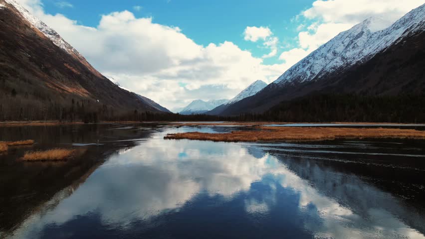 Drone Shot Coasting Over Mirror Like Water With Reflection Of Mountains In Distance In Alaska