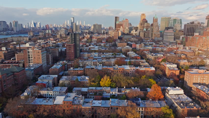 Aerial view of low rise residential buildings and colorful autumn trees in Brooklyn with Manhattan skyline in the background