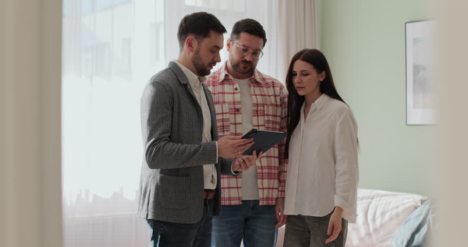 Male real estate agent showing young couple apartment plan using electronic tablet. Home buying concept.