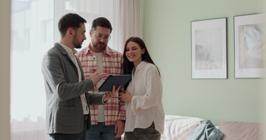 Male real estate agent showing young couple apartment plan using electronic tablet. Home buying concept.