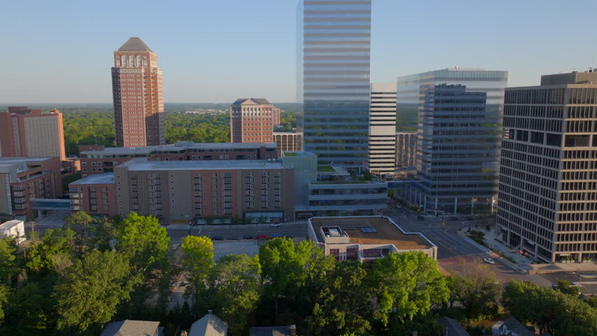 Aerial push-in shot toward contemporary condos and sleek modern office buildings in downtown Clayton, St. Louis, Missouri. The dynamic cityscape and architectural contrast shine on a beautiful day