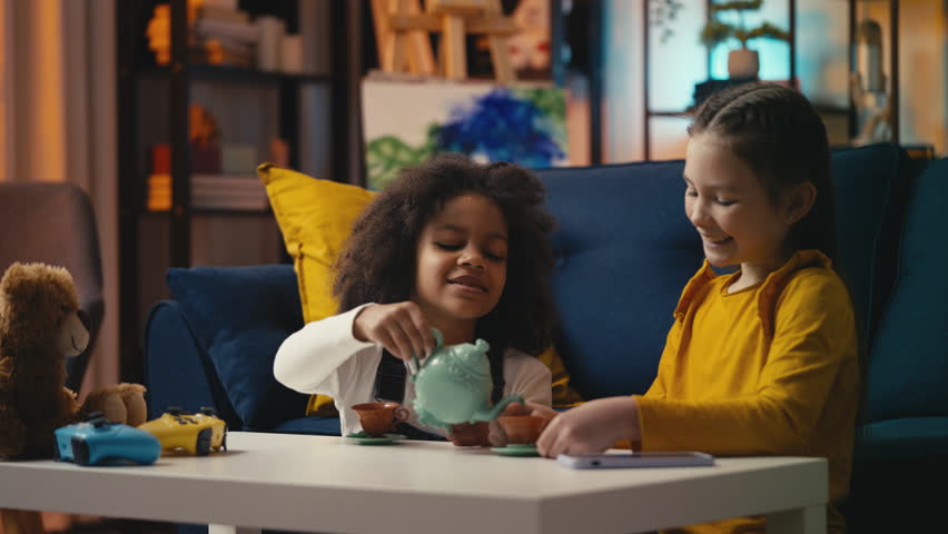 Cheerful multiethnic little girls playing a tea party game, enjoying childhood