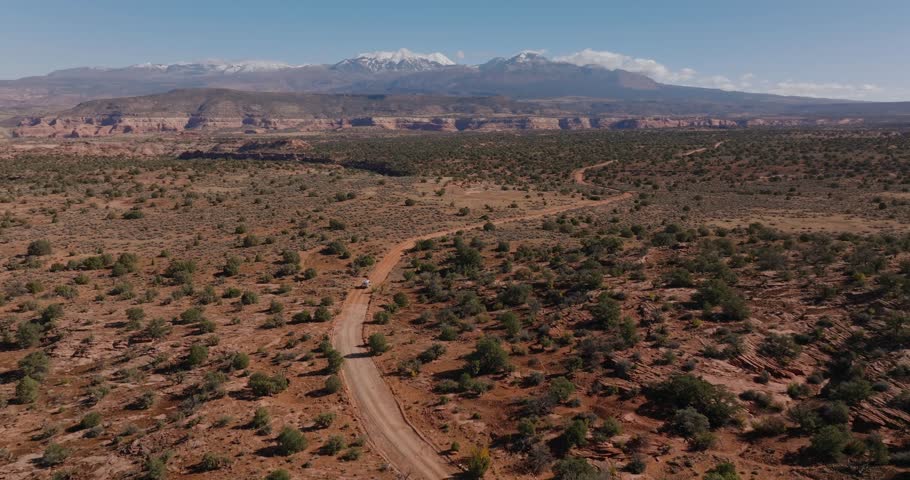 Vehicle makes its way across vast stretch of desert road, mountains in distance