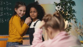 Two multiethnic schoolgirls gossiping about their lonely classmate in the class - Powered by Shutterstock - Get 15% off with code: PIKWIZARD15
