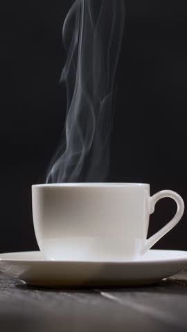 White cup with coffee or tea on black background. Hot cup of coffee with steam rising. Slow motion vertical shot