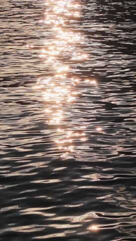 Vertical shot. Peaceful sunrise over shimmering water in serene natural setting near the shore. Reflection of sunlight on sea surface
