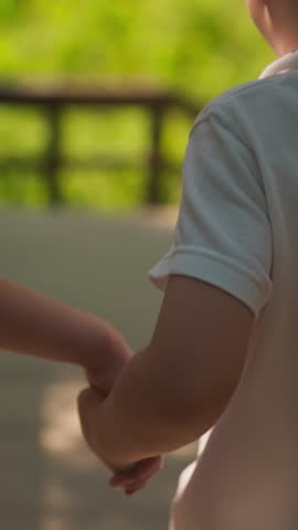 Little girl holds toddler boy hand walking together along overpass in forest closeup. Children enjoy summer and friendship at countryside nature