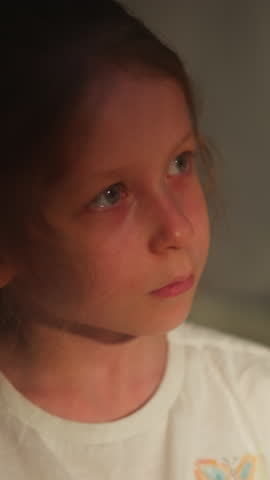 Child with watery eyes in semi-dark room closeup. Little girl cries suffering from domestic violence on blurry background. Sad kid with tears on face