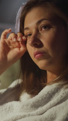 Upset woman wipes tears from corners of eyes with finger sitting in armchair at night in premise. Sad news that disturbed holiday. Depressive state slow motion