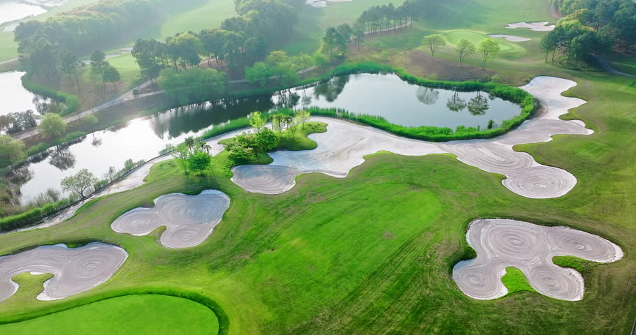 Aerial view of golf course with lake, sand trap, and green grass on a sunny day