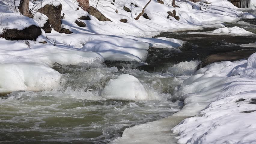 Slow motion video of stream, swollen from  early spring melt, cascading over rocks.  Rising spring temperatures begin to melt the snow and ice in a creek's watershed.