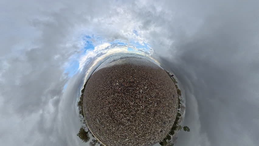 Slow motion, Spherical panorama of waves approaching a pebble beach, with frothy sea foam spreading across the surface, creating a Tiny Planet effect under a cloudy sky