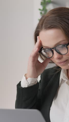 In a busy office, a stressed businesswoman multitasks by juggling a phone call and working on her laptop. Her skills in handling pressure are evident, but constant communication may risk burnout