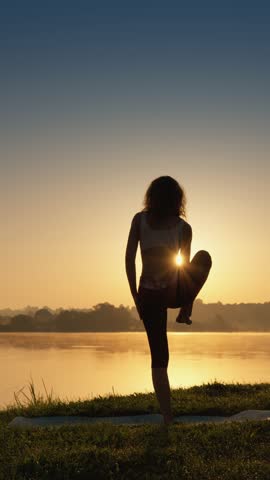 A stunning silhouetted yoga pose by the serene water, beautifully set against the backdrop of a mesmerizing sunset. This scene evokes feelings of peace, tranquility, and harmony with nature