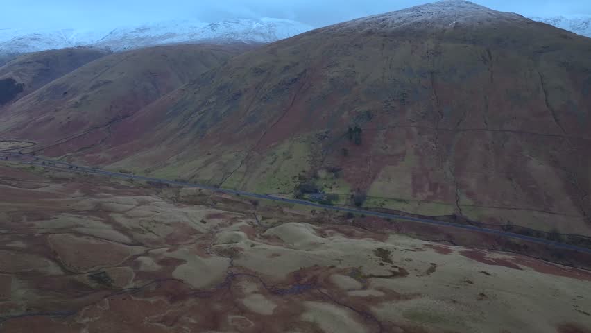 Flight towards mountain road and snow dusted mountains. Lake District, Cumbria, UK.