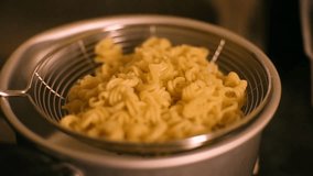 Cooked fusilli pasta being drained in a metal strainer held over a cooking pot. - Powered by Shutterstock - Get 15% off with code: PIKWIZARD15