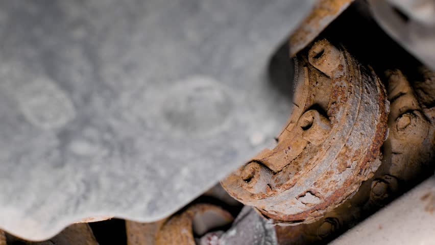 Close up of rusty bolts and driveline parts under a used car. Rotating movement shot in 4k.