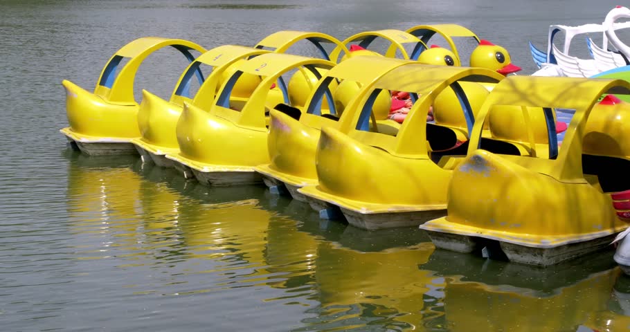 Water duck boat on the amusement park pond. The yellow boat shaped like a duck floats peacefully on calm water.