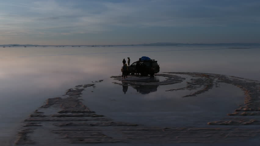 Uyuni Salt Flats (Spanish: Salar de Uyuni) in Bolivia, aerial view with drone orbiting group of tourists exploring the salt flats at sunrise. 