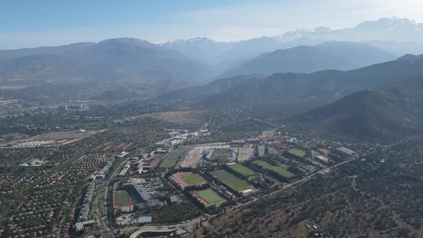 High-altitude perspective showcasing a stadium and surrounding sports fields nestled within a picturesque mountain valley
