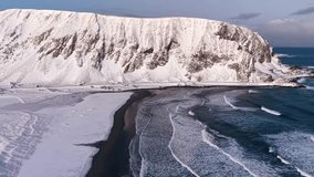 Aerial drone footage of a Norwegian shoreline with mountain and a road during winter time while sun is shining. The road and mountain is on the coast of ocean blue sea water that has big waves. - Powered by Shutterstock - Get 15% off with code: PIKWIZARD15