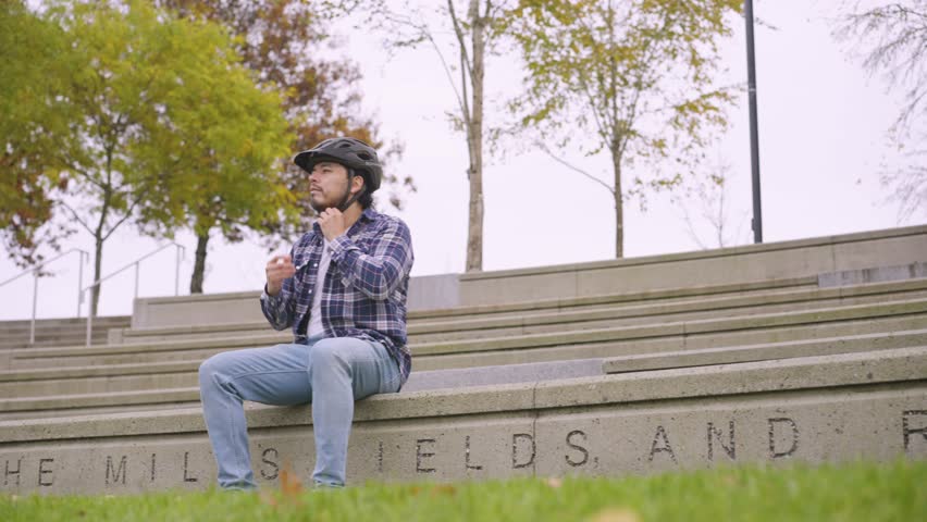 a man takes off his bicycle helmet while sitting in a park.
