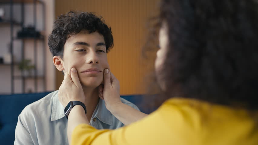 Happy mother pinching the cheeks of her teen son, feeling proud of her child