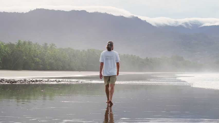 A young boy leisurely strolls along the beautiful Uvita Beach, relishing the breathtaking nature found in Costa Ricas Marino Ballena National Park