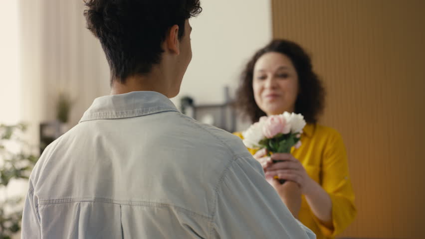 Caring teen son presenting flowers to his loving mom, Mother's Day gift