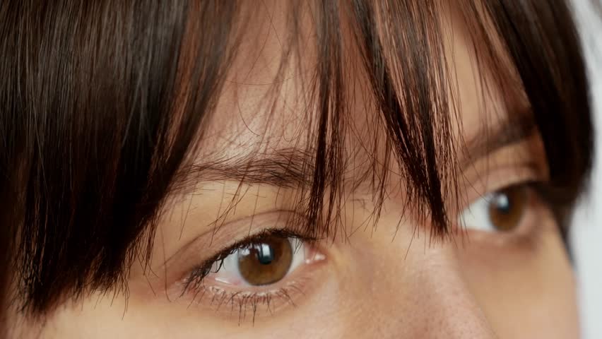 Close-up of a girl with brown eyes blinking and looking away, her face half hidden and her gaze full of emotion.