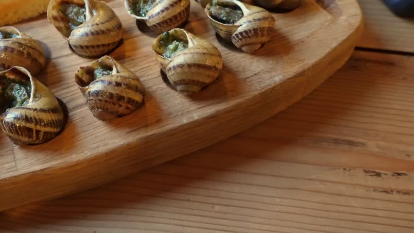 Closeup of gourmet escargot preparation on wooden platter in warm kitchen light