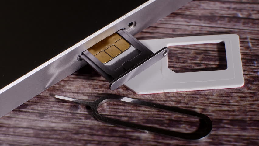 Closeup shot showing the sim card slot of a silver colored smartphone. The tool needed to open it. Communication. Modern technology. Wood background. Camera slowly moving around.