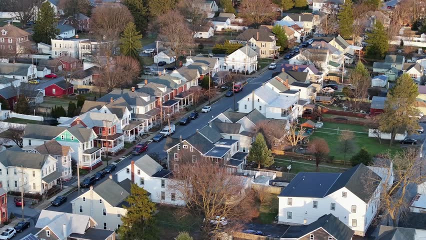 Charming small town in USA with leafless trees during golden sunset in winter. Aerial establishing wide shot. Straight Main street with parking cars in quiet housing area.