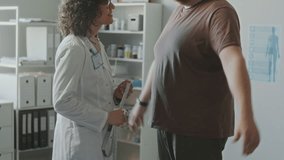 Female doctor measuring body circumference of obese man, then giving supportive words and advice on weight loss during health checkup in medical office - Powered by Shutterstock - Get 15% off with code: PIKWIZARD15