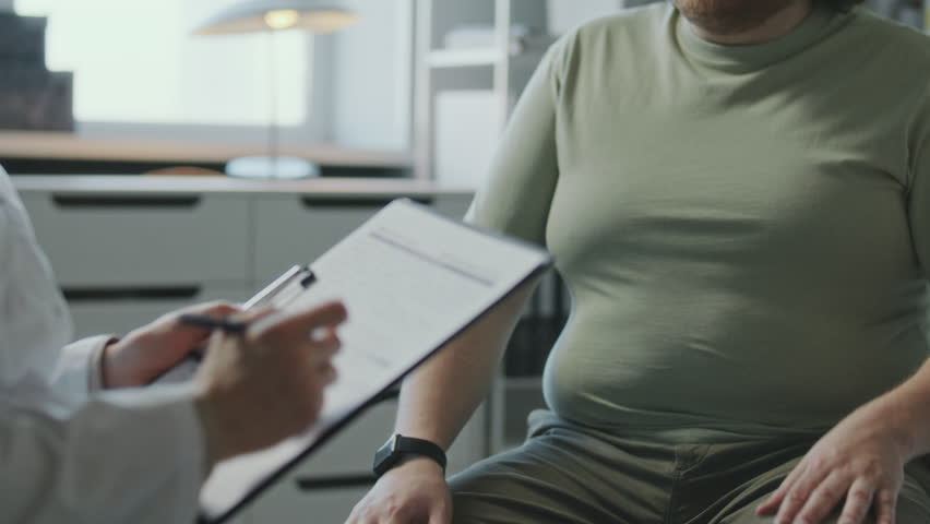 Overweight patient touching his stomach and consulting doctor about weight loss during visit to clinic. Midsection shot