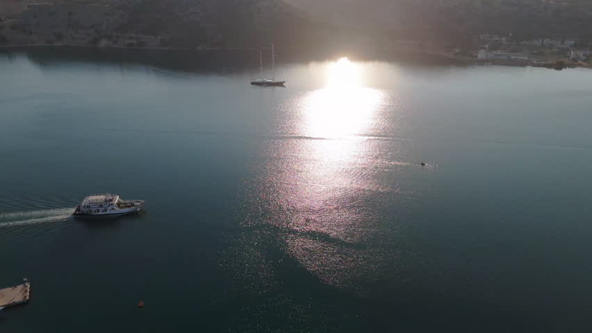 Drone tracking left past ferry in open waters of Argostoli, Kefalonia, Greece, the golden reflections at sunset
