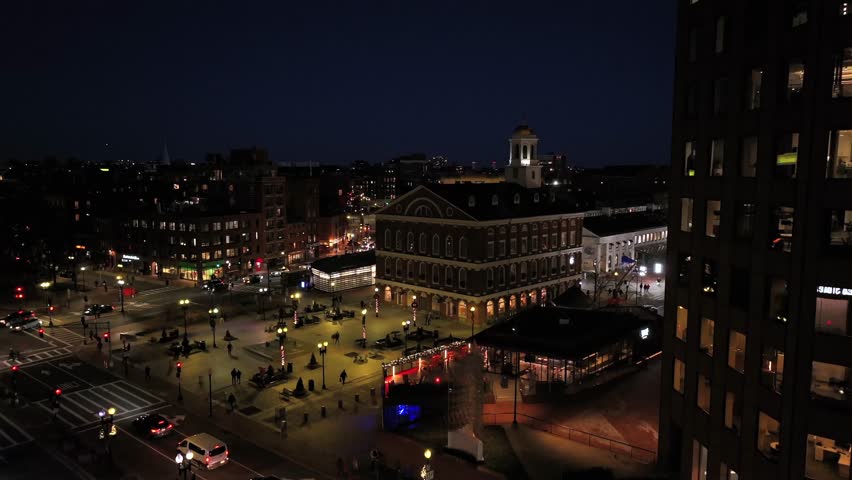 Aerial approaching shot of Faneuil Hall Marketplace in Boston City with walking people in square. Warm lighting lantern at night. American metropolis with traffic on street. Wide shot.