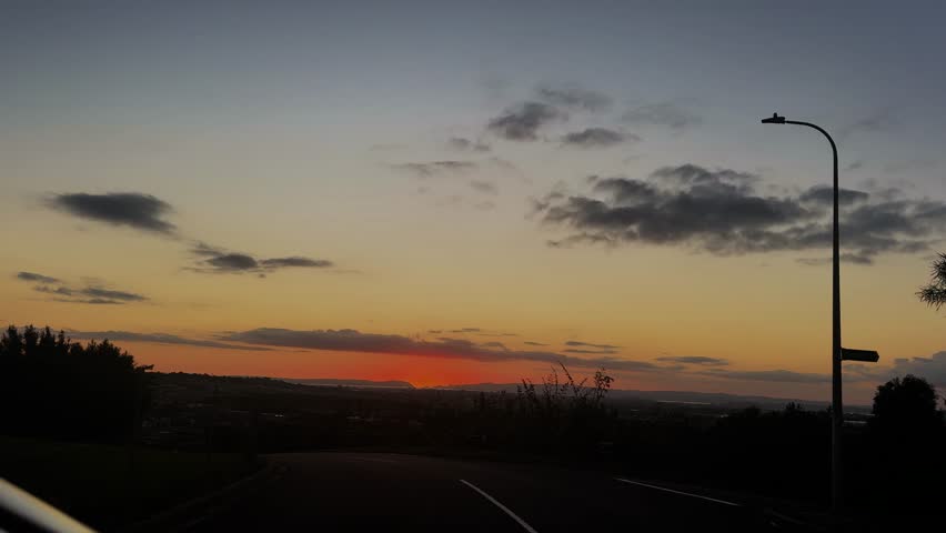 The sun is setting slowly on the horizon of hills and ocean in Auckland, New Zealand.