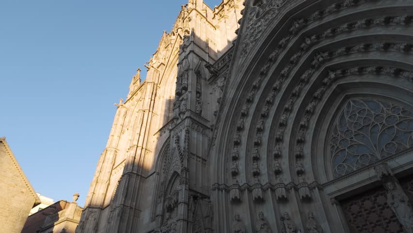Grand view of the Gothic Cathedral of Barcelona with towering spires and intricate details, sunlight on top and shadow across archway