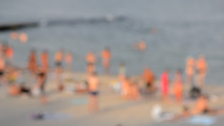 Lots of people on beach by sea on summer evening. Many men and women in bathing suits and swimming trunks on sandy beach on seashore. Rest and relaxation on beach. People sunbathing Blurred background
