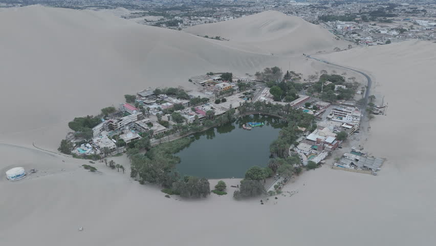 Drone shot revealing the city of Huacachina in Peru behind the dunes on a cloudy morning during the mist LOG