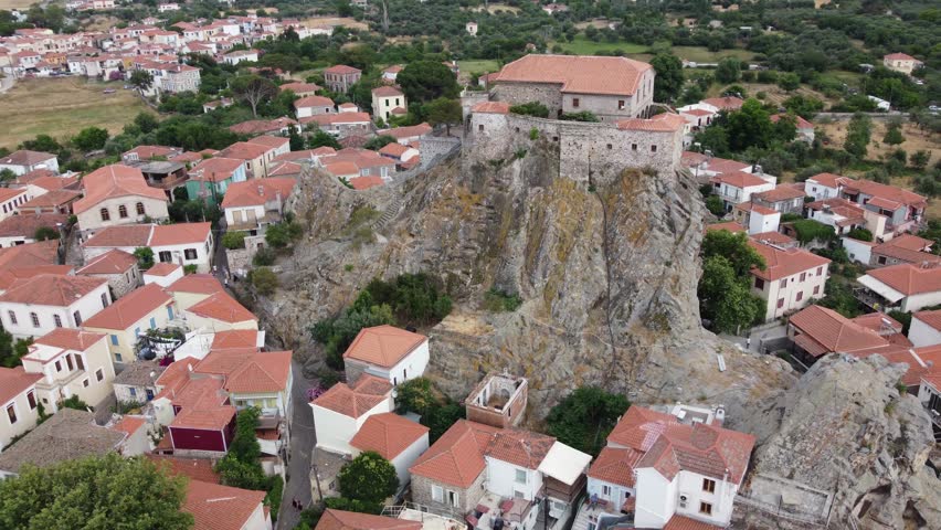 Virgin Mary Greek Orthodox church courtyard at top of rock surrounding Petra village traditional houses with terracotta roofs, Aegean Sea, Lesvos, Drone view